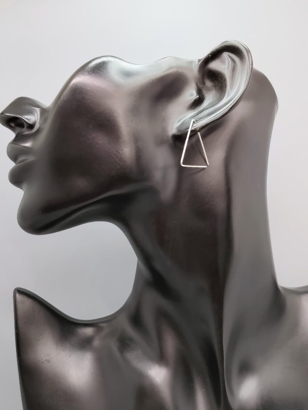 Frontale Nahaufnahme eines Models, das einen der offenen Dreieck-Drahtohrringe trägt, der minimalistisch am Ohrläppchen hängt. Creolen dreieckig - silber, gold, rosegold