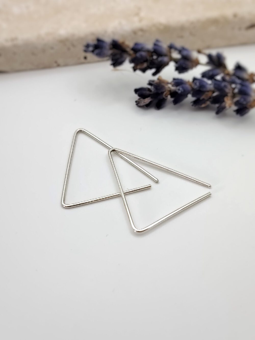 Nahaufnahme von zwei minimalistischen, ineinander liegenden, offenen Dreieck-Drahtohrringen aus poliertem 935 Silber vor weißem Hintergrund. Creolen dreieckig - silber, gold, rosegold