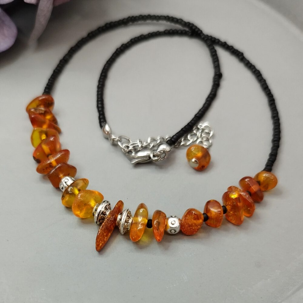 Nahaufnahme der Choker-Kette, Fokus auf die Bernsteinsplitter. Detailreiche Handarbeit. Warme Bernsteinsplitter treffen auf edles Tibetsilber. Bernstein Kette schwarz-silber