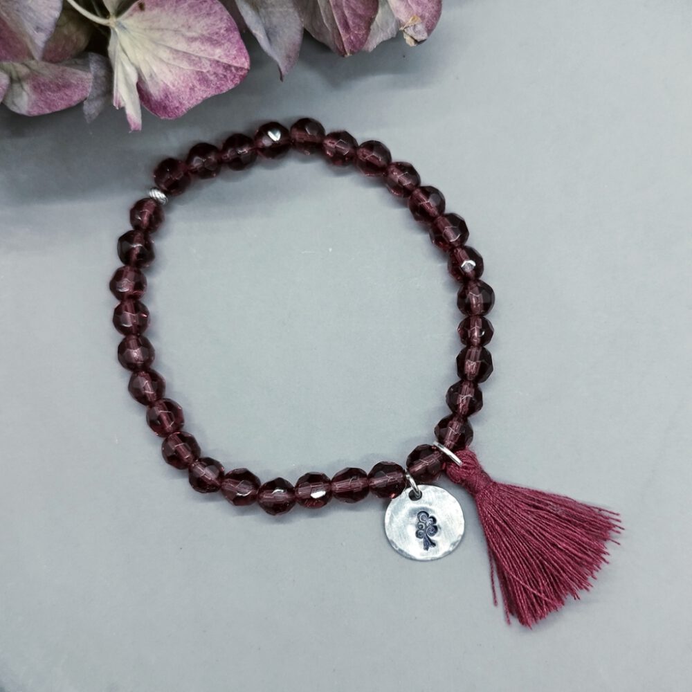 Nahaufnahme des silbernen Anhängers mit dem von Hand eingravierten Lebensbaum. Armband weinrote Kristalle, elastisch