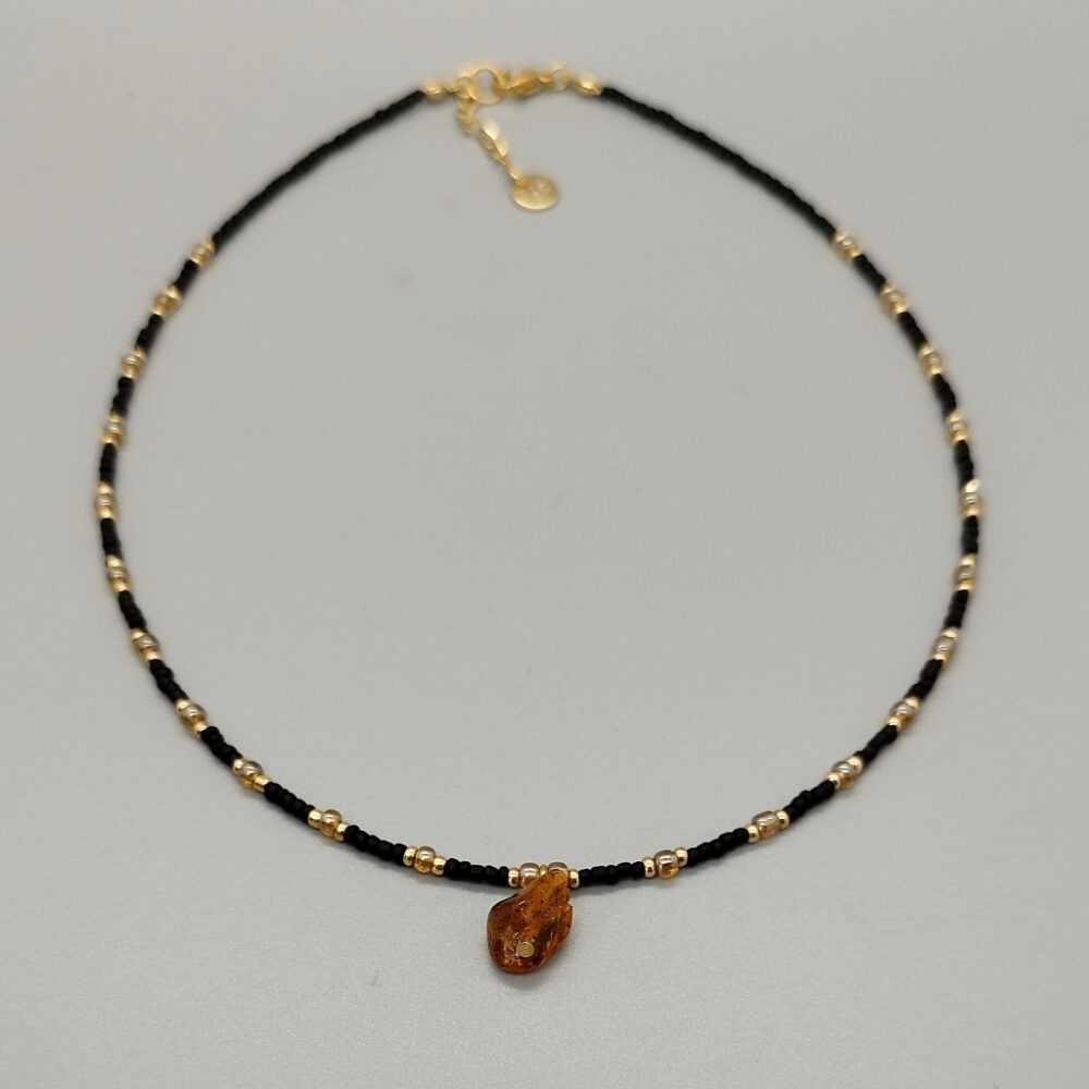 Die Choker-Kette liegt auf einem grauen Hintergrund und zeigt den Kontrast zwischen Schwarz und Gold. Kette schwarz gold mit Bernstein Anhänger