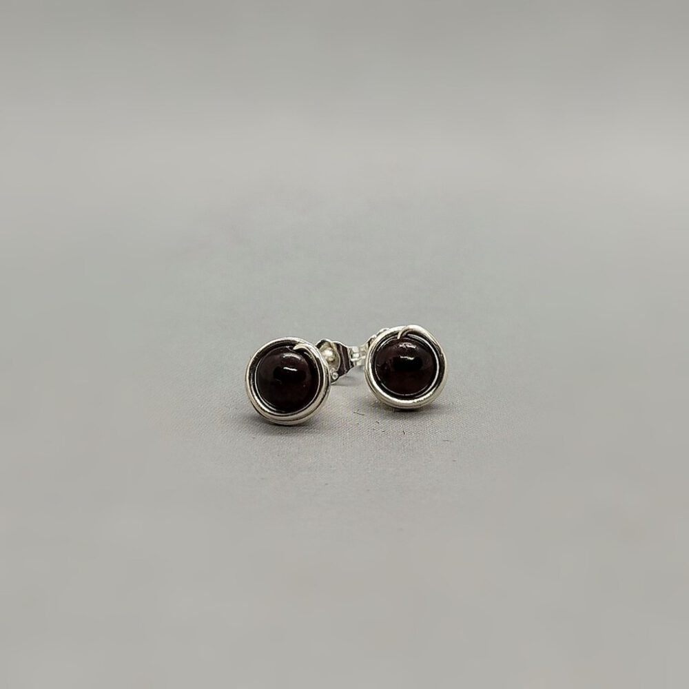 Handgefertigte Granat-Ohrstecker auf grauem Hintergrund. Ohrstecker Granat 935 Silber