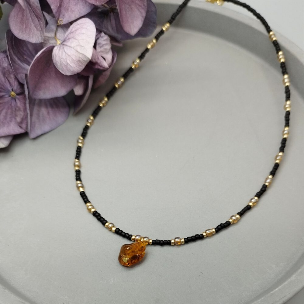 Kette aus kleinen schwarzen und goldenen Perlen mit einem Bernstein Anhänger Kette schwarz gold mit Bernstein Anhänger