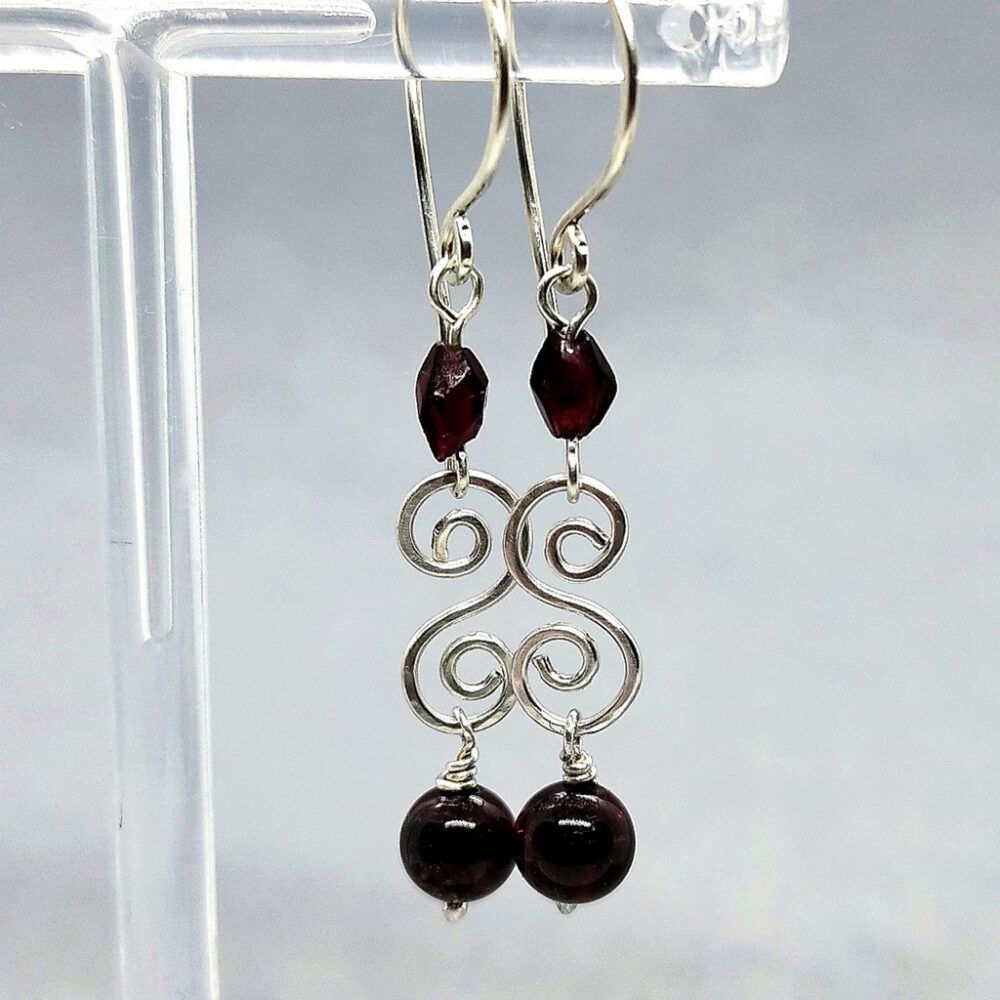 Ohrhänger mit granatfarbenem Kristall und Granatperle in eleganter Nahaufnahme. Granat-Ohrhänger mit 935 Silber-Doppelspirale