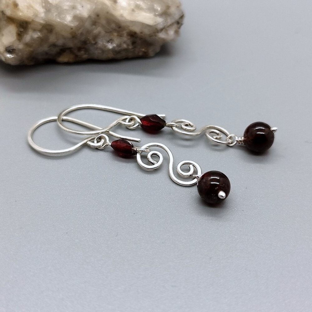 Ohrhänger mit schimmerndem Granatstein und kunstvoller Silberverarbeitung. Granat-Ohrhänger mit 935 Silber-Doppelspirale