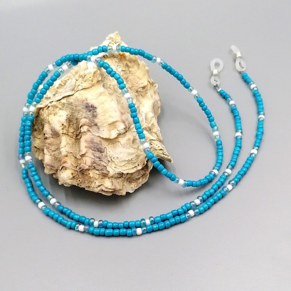 Brillenkette dekorativ über eine Muschel drapiert Brillenkette in Türkis & Weiß – handmade