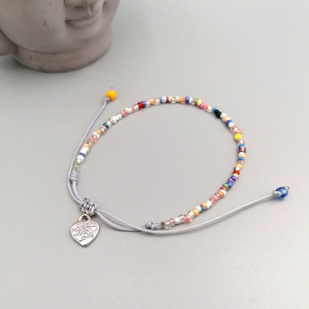 Buntes Boho Armband mit Herzanhänger auf hellem Hintergrund Buntes Boho Armband mit Herzanhänger