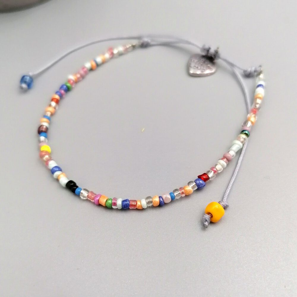 Nahaufnahme bunte Rocailles mit silberfarbenem Herz Buntes Boho Armband mit Herzanhänger
