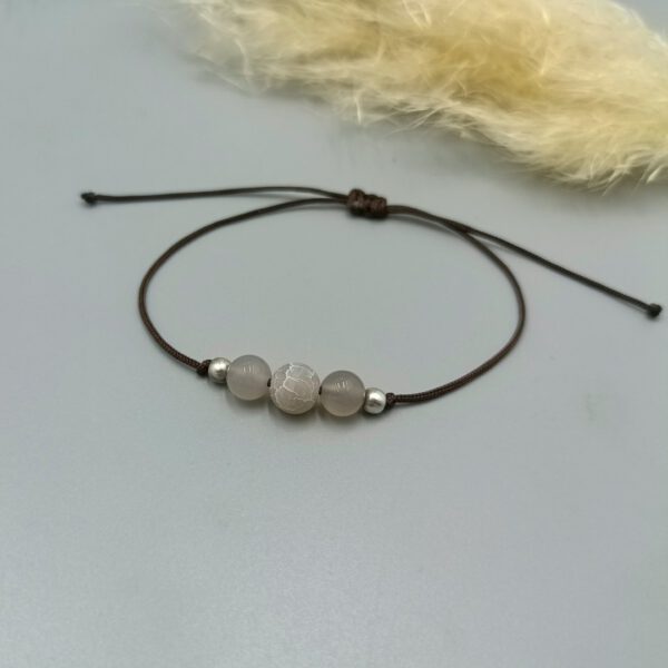 Armband aus braunem Nylonfaden mit mittiger grauer Achatperle auf hellem Hintergrund. Armband mit Achat & Silberperlen